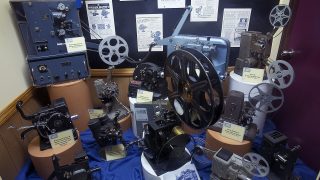 Vintage film projectors and reels in a display case.