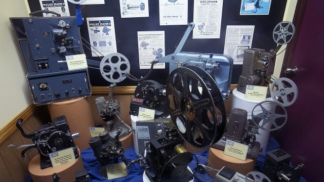 Vintage film projectors and reels in a display case.