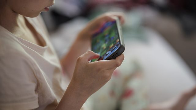 A child looks at a smartphone while sitting on a bed at home.