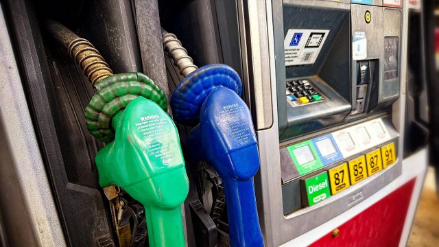 Fuel nozzles at a gas station pump, including a green diesel nozzle.