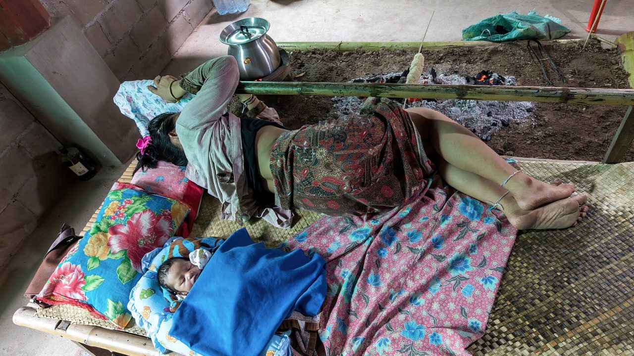Mother and newborn sleeping on a bamboo bed near a campfire in a house in Don Det Laos