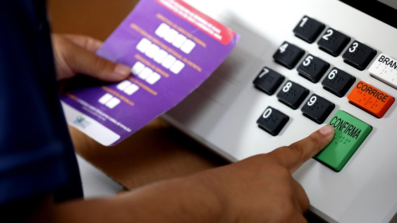 A finger presses the green confirm key on a Brazilian electronic voting machine during a 2022 demonstration.