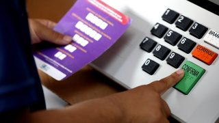 A finger presses the green confirm key on a Brazilian electronic voting machine during a 2022 demonstration.